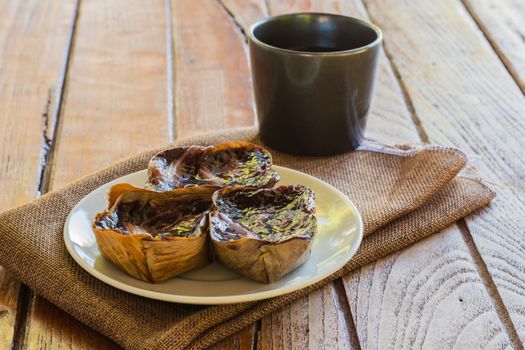 Black sticky rice cake Nian Gao in dried banana leave cup on white plate and wooden table. Traditional snack in Chinese new year.