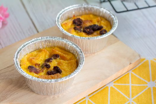 Bread pudding with black rasins in round foil cup on wooden tray. Delicious custard for coffee times.