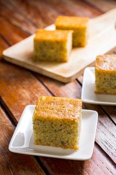 Close up square cut of homemade sweet and solf banana cake on white plate on wooden table. Delicious and healthy bakery.