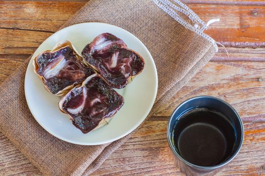 Black sticky rice cake Nian Gao in dried banana leave cup on white plate and wooden table. Traditional snack in Chinese new year.