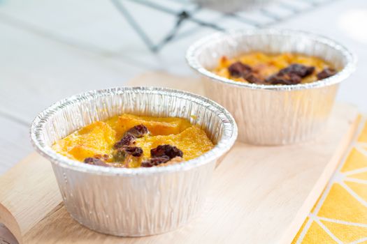 Bread pudding with black rasins in round foil cup on wooden tray. Delicious custard for coffee times.