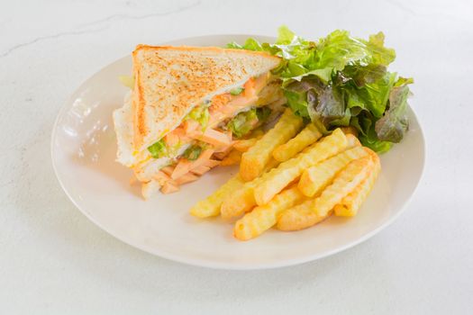 Sandwich with sausage, mayonnaise and ketchup on white plate with french fries and fresh lettuce. Fast food concept.