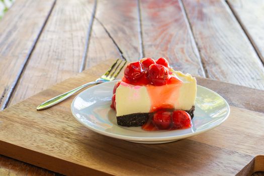 Cherry cheese pie cake in white plate and metal fork on wooden table.