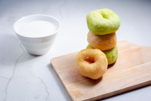 Vanilla and pandan doughnut on wooden chopping board with cup of hot milk. Breakfast concept.