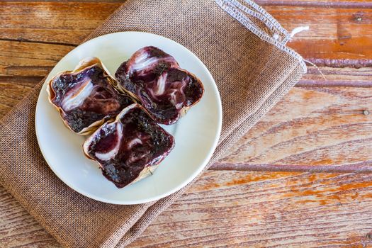 Black sticky rice cake Nian Gao in dried banana leave cup on white plate and wooden table. Traditional snack in Chinese new year.