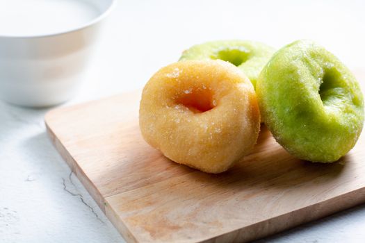 Vanilla and pandan doughnut on wooden chopping board with cup of hot milk. Breakfast concept.