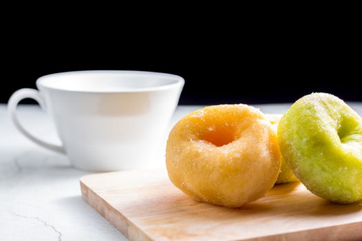 Vanilla and pandan doughnut on wooden chopping board with cup of hot milk. Breakfast concept.