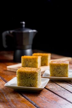 Close up square cut of homemade sweet and solf banana cake on white plate on table with solf focus black moka pot. Delicious and healthy bakery.