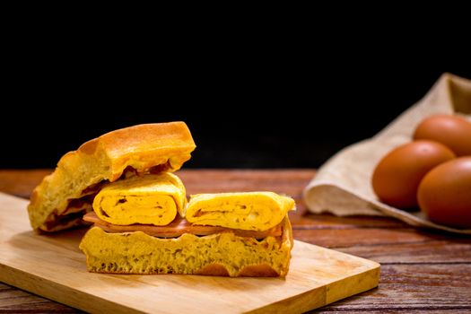 Waffle sandwich with egg and chicken ham on chopping board on wooden table and black background. Homemade food concept.