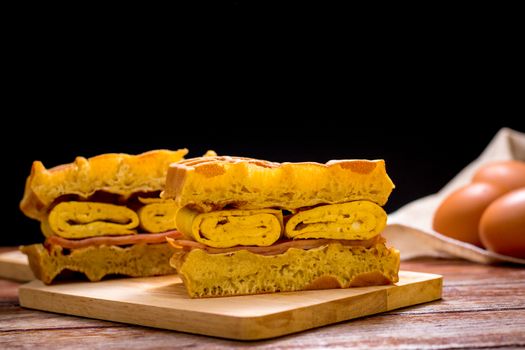 Waffle sandwich with egg and chicken ham on chopping board on wooden table and black background. Homemade food concept.