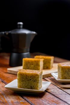 Close up square cut of homemade sweet and solf banana cake on wooden chopping board and fork on table with solf focus black moka pot. Delicious and healthy bakery.