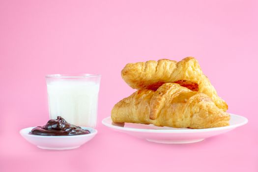 Two croissants on white dish and glass of fresh milk on pink back ground with copy space for your text. Breakfast concept.