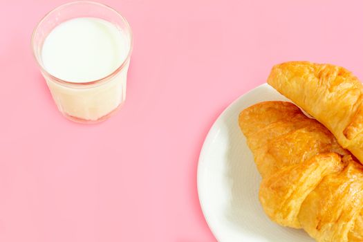 Two croissants on white dish and glass of fresh milk on pink back ground with copy space for your text. Breakfast concept.