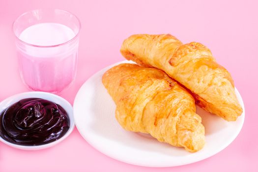 Two croissants on white dish and glass of fresh milk on pink back ground with copy space for your text. Breakfast concept.