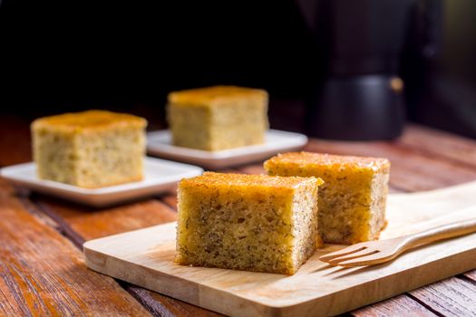 Close up square cut of homemade sweet and solf banana cake on wooden chopping board and fork on table. Delicious and healthy bakery.