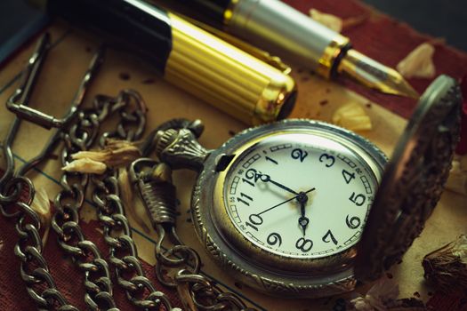 Vintage pocket watch and brass pen on old book. At 8 o'clock in morning. Education and vintage style concept.