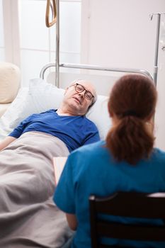 Back view of nurse sitting on chair talking with pensioner in nursing home.