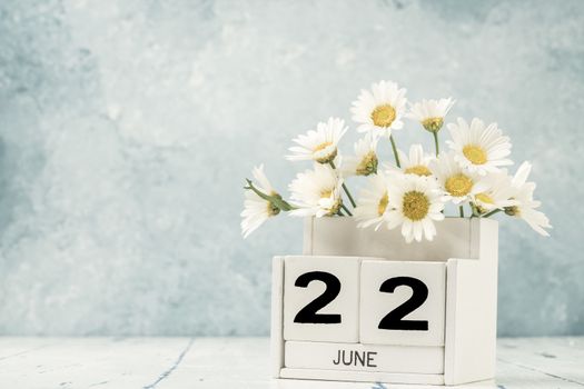 White cube calendar for june decorated with daisy flowers over blue background with copy space