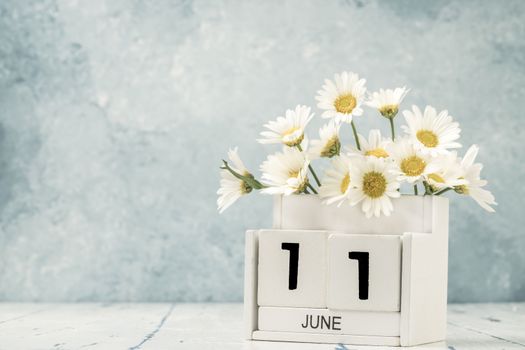 White cube calendar for june decorated with daisy flowers over blue background with copy space