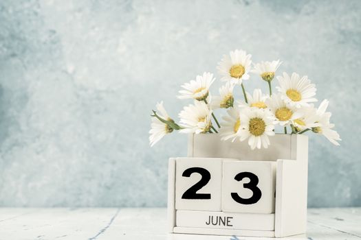 White cube calendar for june decorated with daisy flowers over blue background with copy space