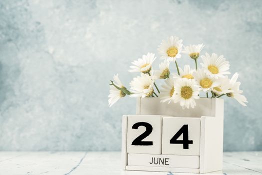 White cube calendar for june decorated with daisy flowers over blue background with copy space