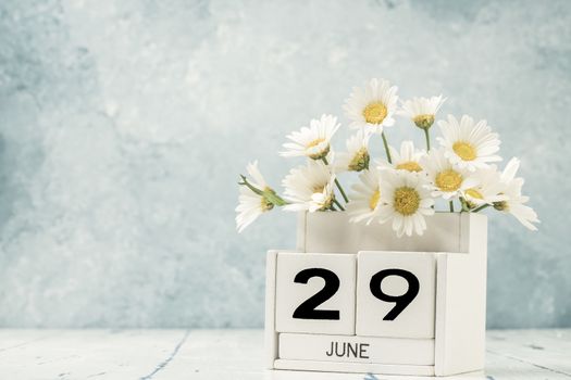 White cube calendar for june decorated with daisy flowers over blue background with copy space