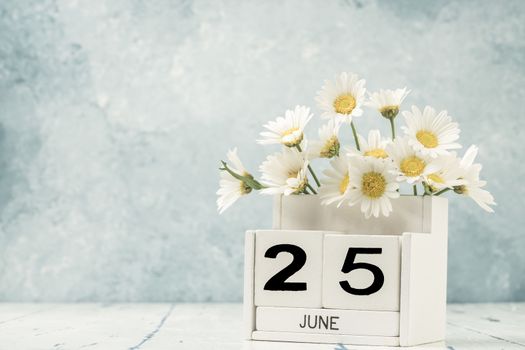 White cube calendar for june decorated with daisy flowers over blue background with copy space