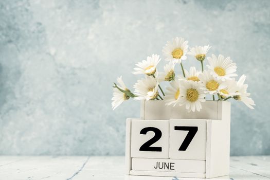 White cube calendar for june decorated with daisy flowers over blue background with copy space