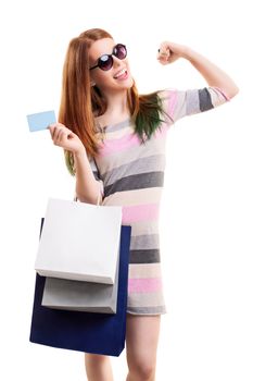 Excited beautiful young girl in a dress with sunglasses, holing shopping bags and a blank card, with raised arm, isolated on white background. Shopping concept, copy space.