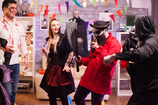 Man dressed up like a pirate holding an axe dancing at halloween celebration with his friends.