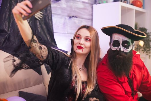 Best friends dressed up like medieval pirate and vampire woman taking selfie at halloween party.