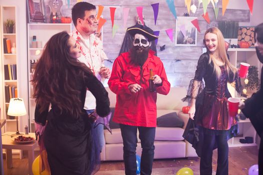 Cheerful young woman dressed up like a vampire with bloody lips at halloween celebration with her funny friends.