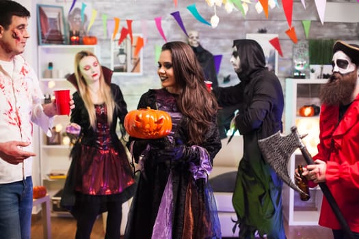 Cheerful woman with a witch costume holding a pumpkin at halloween party.