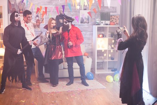 Back view of witch taking photos of spooky group of people at halloween party.