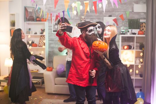 Bearded medieval pirate taking a selfie with beautiful vampire woman at halloween party. Spooky pumpkin.