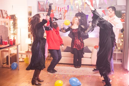 Group of friends dancing with hands up while celebrating halloween in their costumes.
