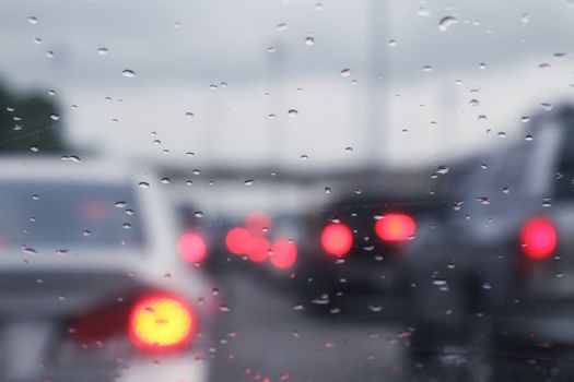 Blurred background traffic car jam and rain drops water on glass with bokeh lighting car