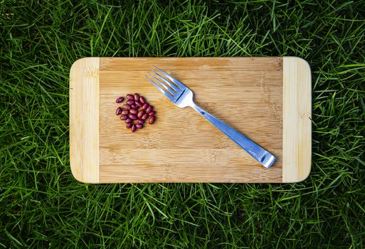 Red kidney beans and a fork, on a wood cutting board, in green grass