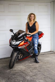 Young blond woman, sitting on a sport motocycle, in front a garage door