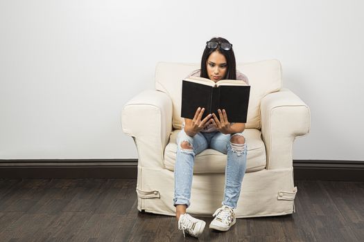 Young woman, sitting on a white couch, deeply lost in reading a  book