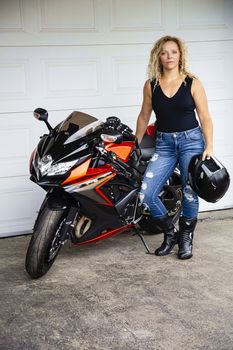 twenty something woman, with curly blond hair, standing beside a sport motocycle, holding a helmet