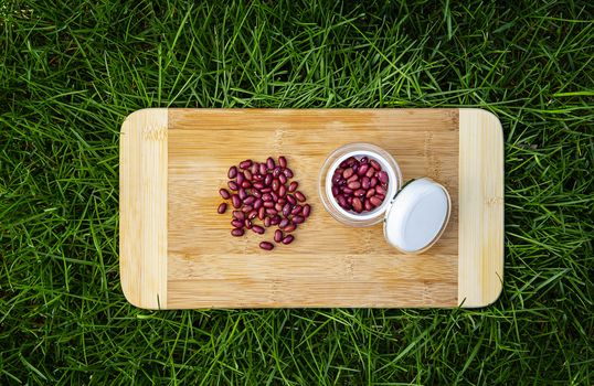 pile of red kidney beans on a wood cutting board, in green grass and small beauty cream container filled with red kidney bean
