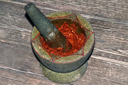 Chili grinding in Mortar stone on wooden background, Mortar and pestle is red chili grinding and garlic for curry ingredients, Thai red curry grinding paste for ingredients sour soup spices in mortar