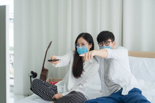 Social distancing.Young Asian people are watching television news. Stay in the bedroom happily. They wear masks to prevent the outbreak of the virus.