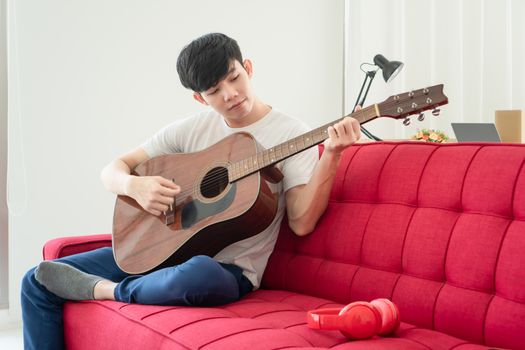 A young Asian man is at home happily. He is unemployed He is playing guitar and singing to relax.