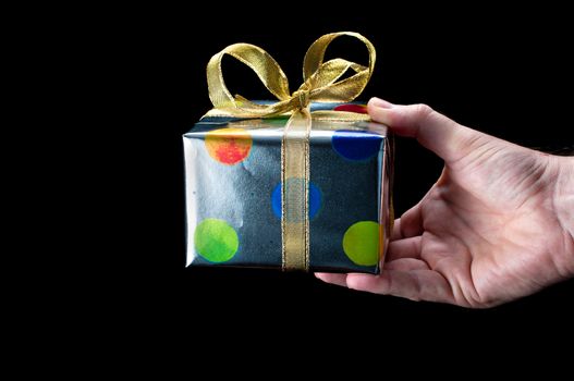Man's hand holding a colorful silver present with a gold bow on a black background