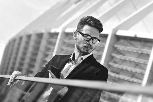 Modern businessman. Confident young man in full suit standing outdoors with cityscape in the background using a smartphone