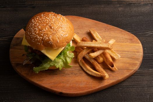 fresh tasty homemade hamburger with fresh vegetables, lettuce, tomato, cheese on a cutting board with French fries. Free space for text