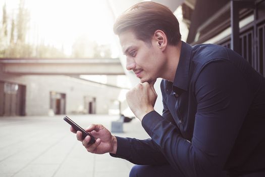 Smiling businessman use a smartphone at street.