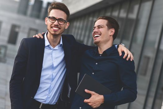 Two smiling colleagues speaking and having fun at street.